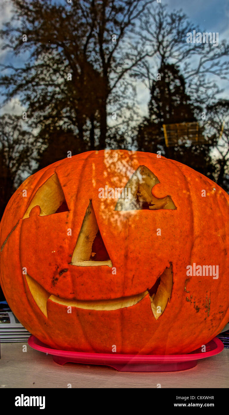 Spooky Halloween pumpkin in a café window with reflected graveyard trees... Stock Photo