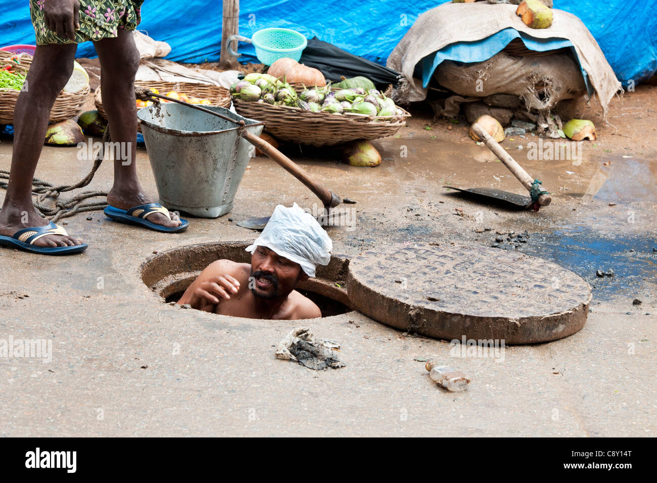 Indian sewage worker coming up from unblocking drains in the street ...