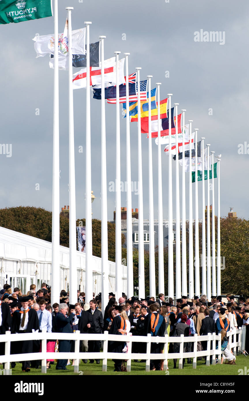 Flag poles showing flags from different countries on Graduation day at Plymouth University.  People wearing academic dress. Stock Photo