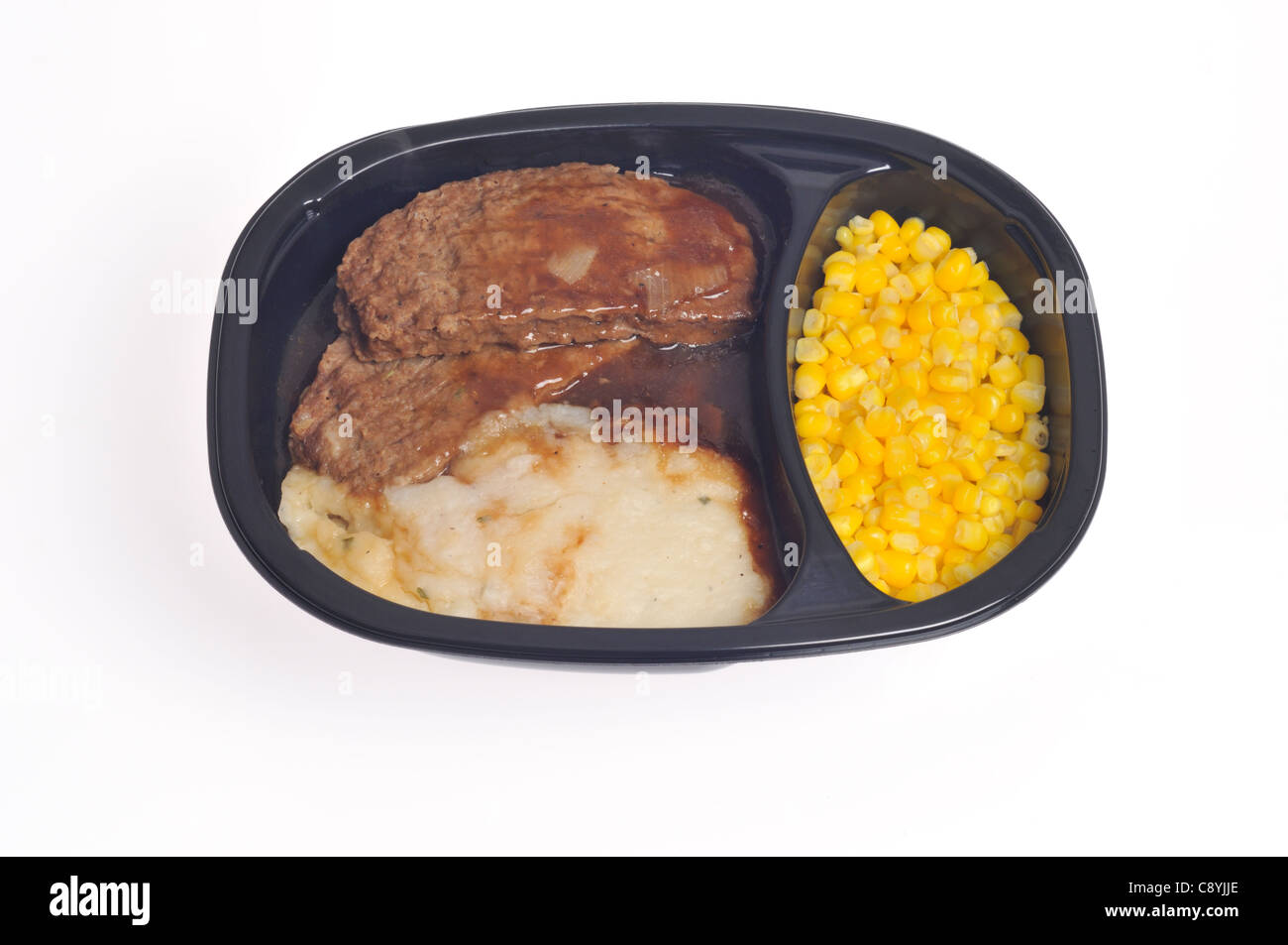 Cooked microwave meatloaf tv dinner with gravy, mashed potatoes and sweet corn in plastic tray on white background cutout. Stock Photo