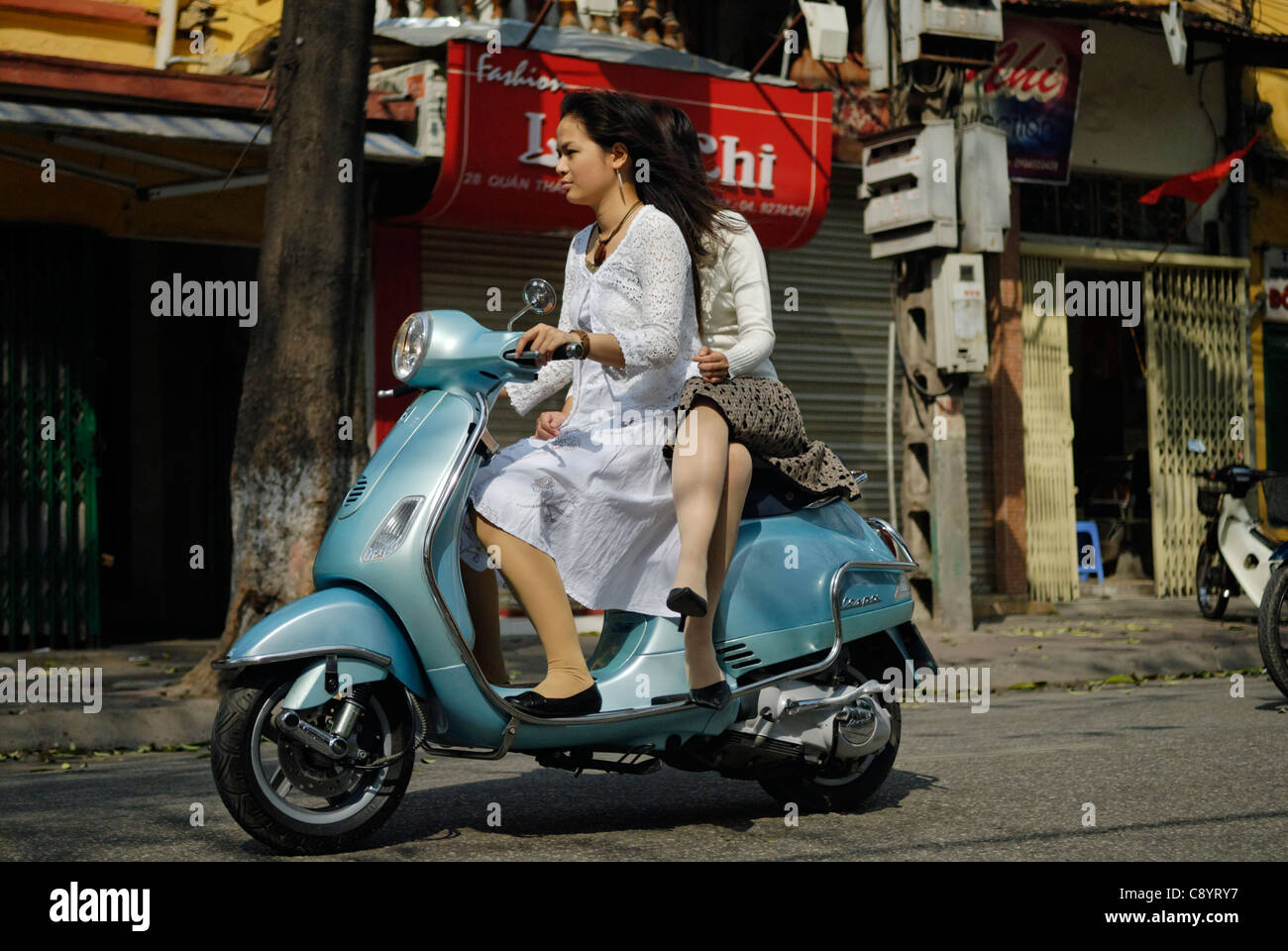 Asia, Vietnam, Hanoi. Hanoi old quarter. Two young dressy vietnamese women riding a Vespa motorbike through Hanoi.... Stock Photo