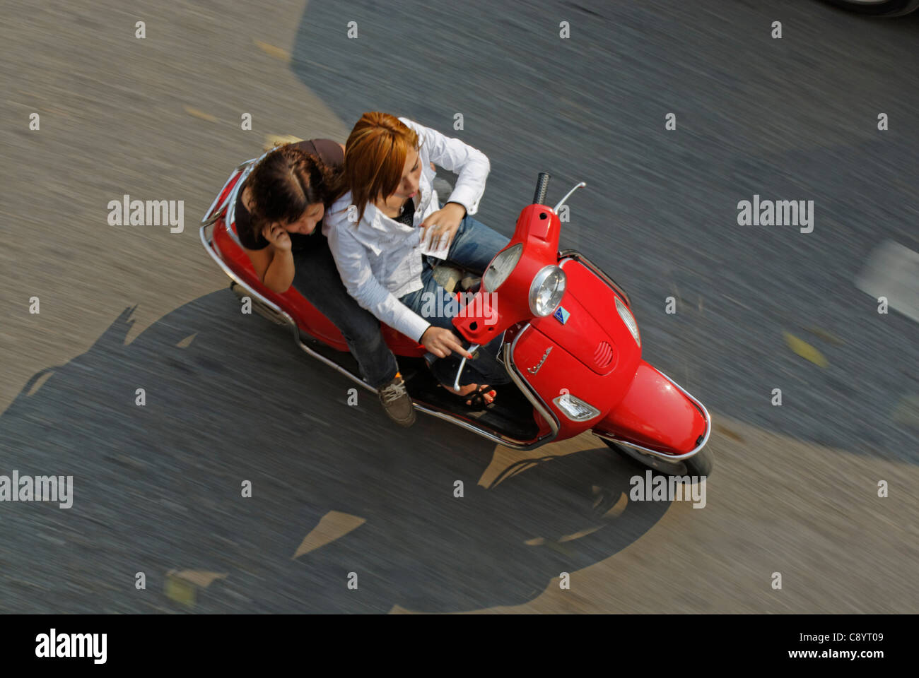 Asia, Vietnam, Hanoi. Hanoi old quarter. Young fashionable vietnamese women riding a red Vespa motorbike through Hanoi.... Stock Photo