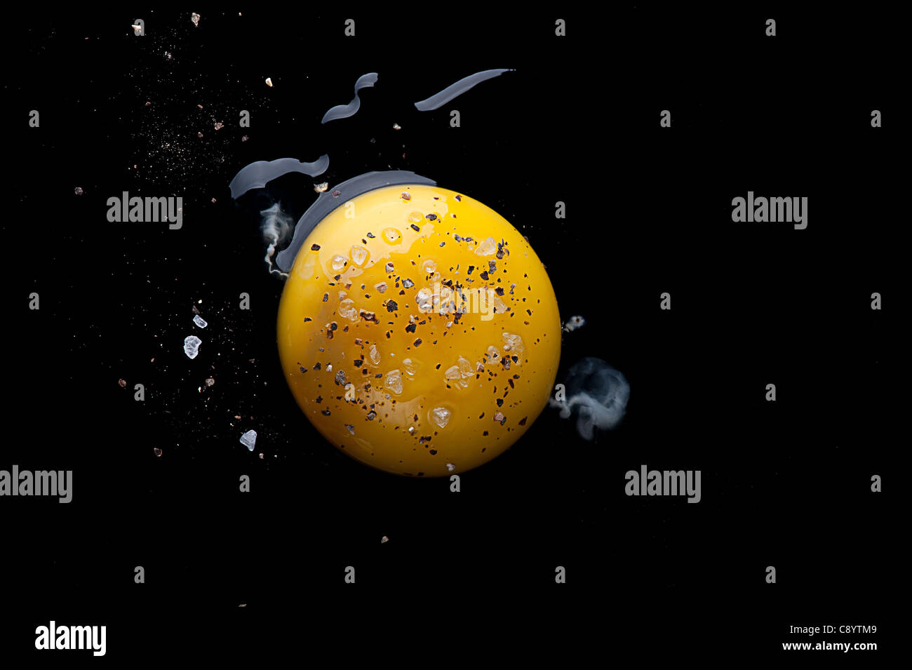 Aerial view of a Raw egg and egg yolk on a black reflecting surface with salt and pepper. Stock Photo