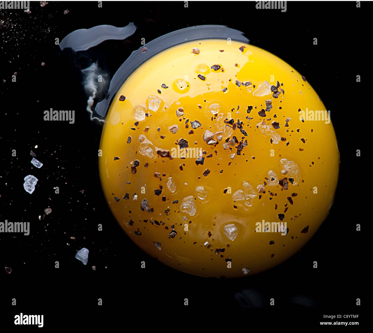 Aerial view of a Raw egg and egg yolk on a black reflecting surface with salt and pepper. Stock Photo