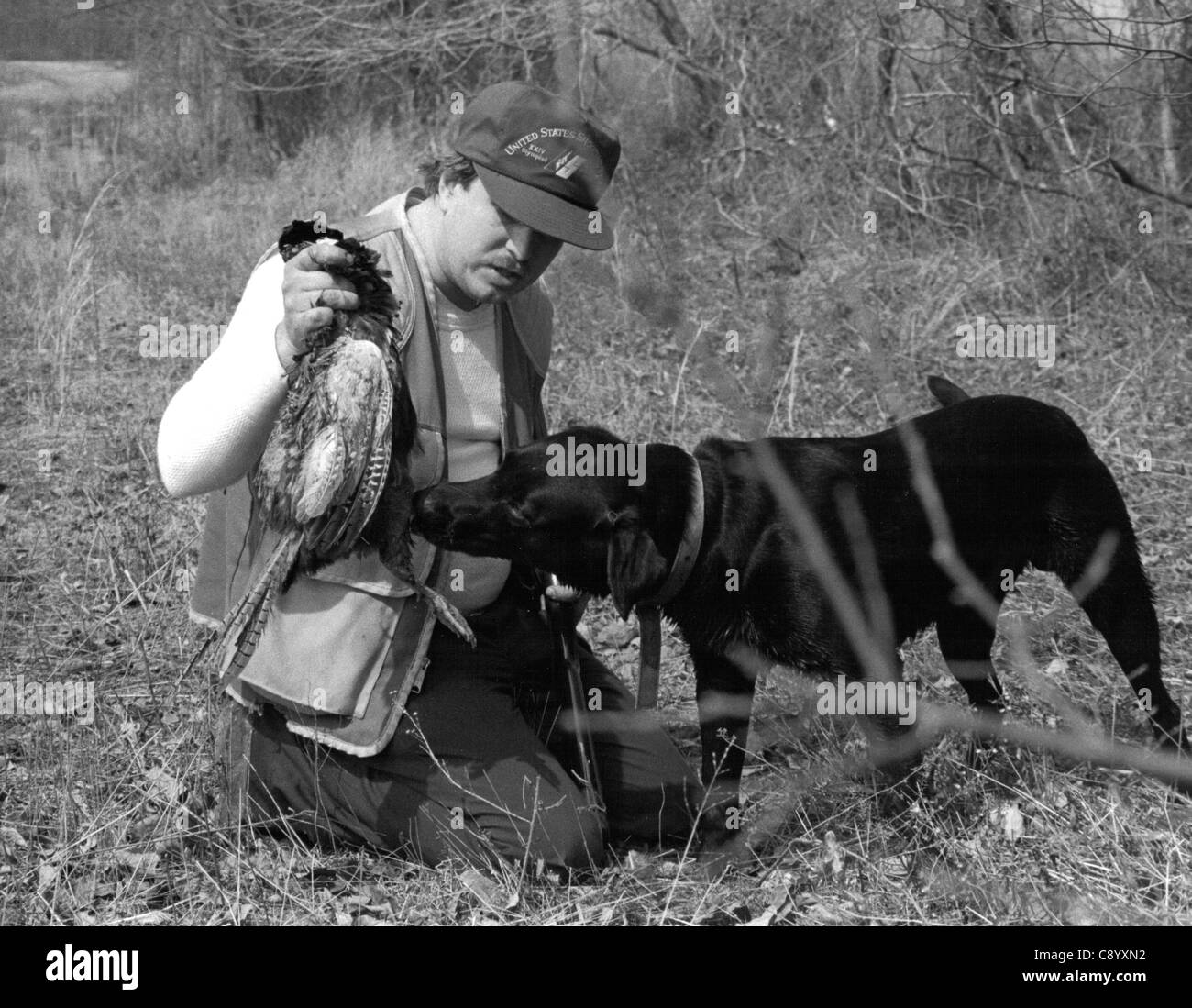 Black and white photo of hunter holding up pheasant with Labrador Retriever looking on Stock Photo