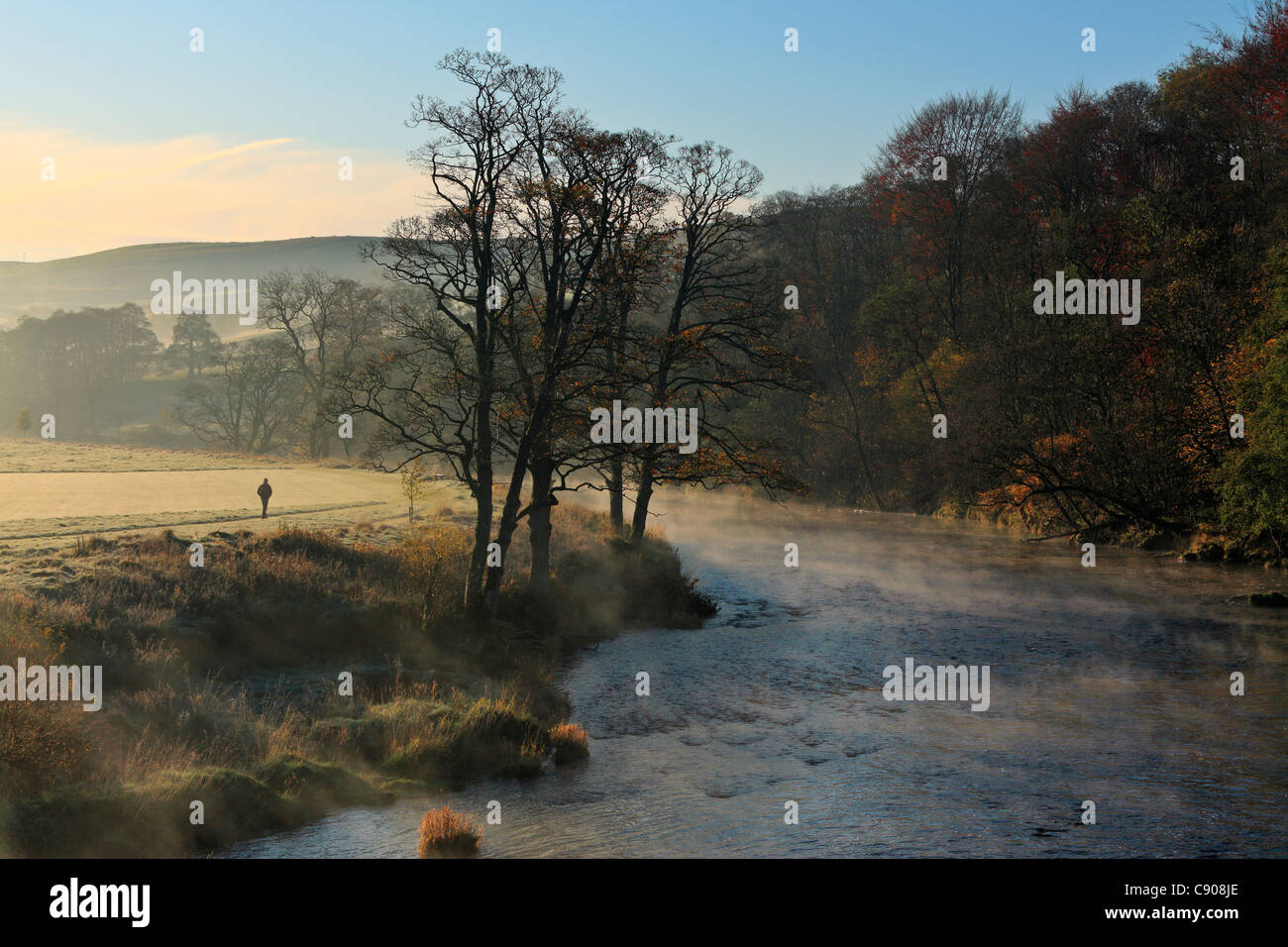 A man walks along the shore of a misty River Wharfe in autumn Stock Photo
