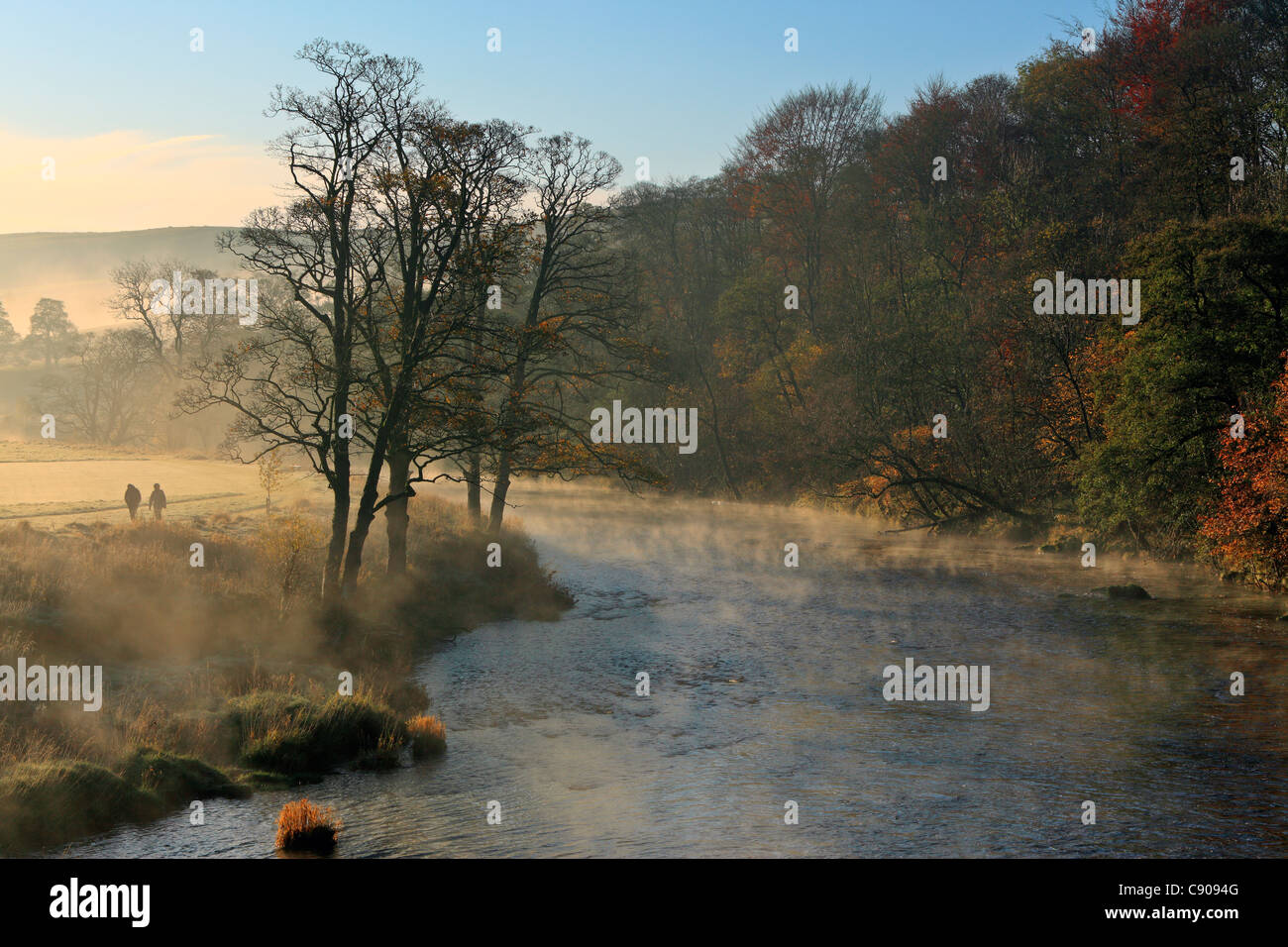 A couple walks along the shore of a misty River Wharfe in autumn Stock Photo
