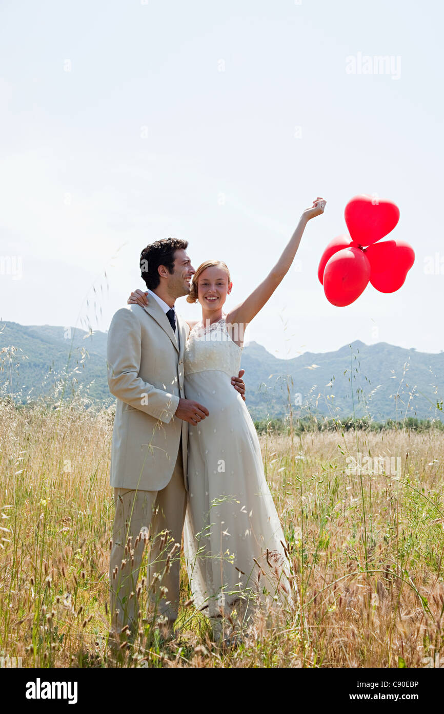 Newlyweds in field with red heart shape balloons Stock Photo - Alamy