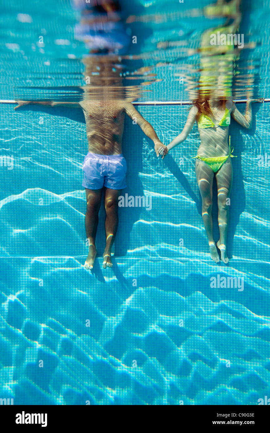 Young couple holding hands in swimming pool, underwater view Stock