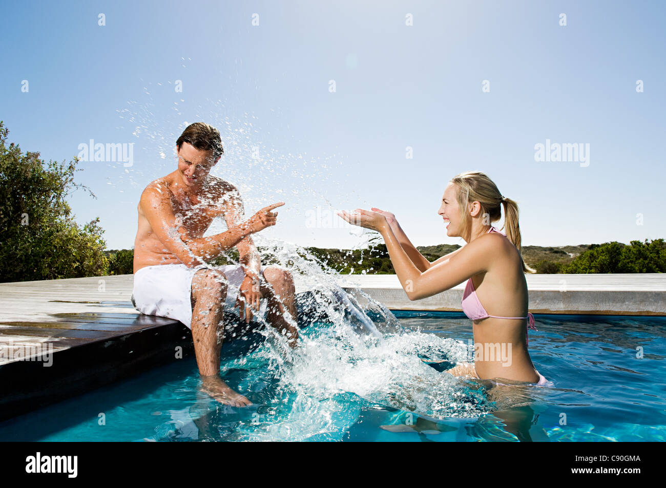 Young couple splashing in swimming pool Stock Photo