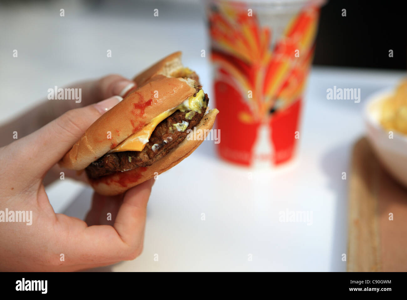 A hand holding a cheese burger with ketchup and soft drink Stock Photo