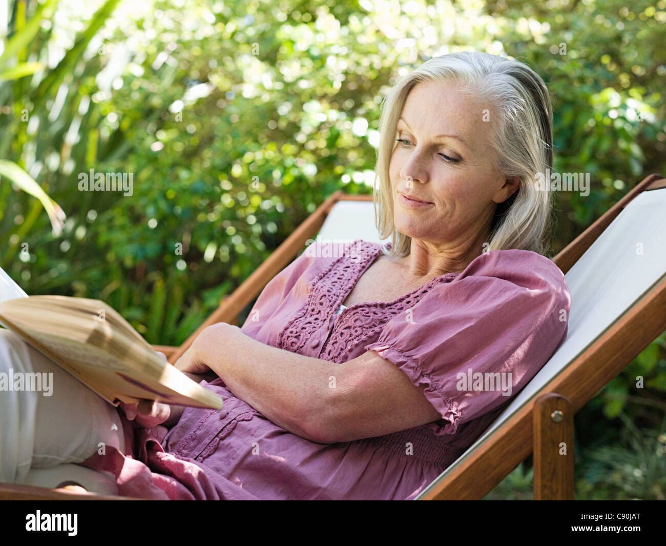 Woman sitting on deckchair in garden with book Stock Photo