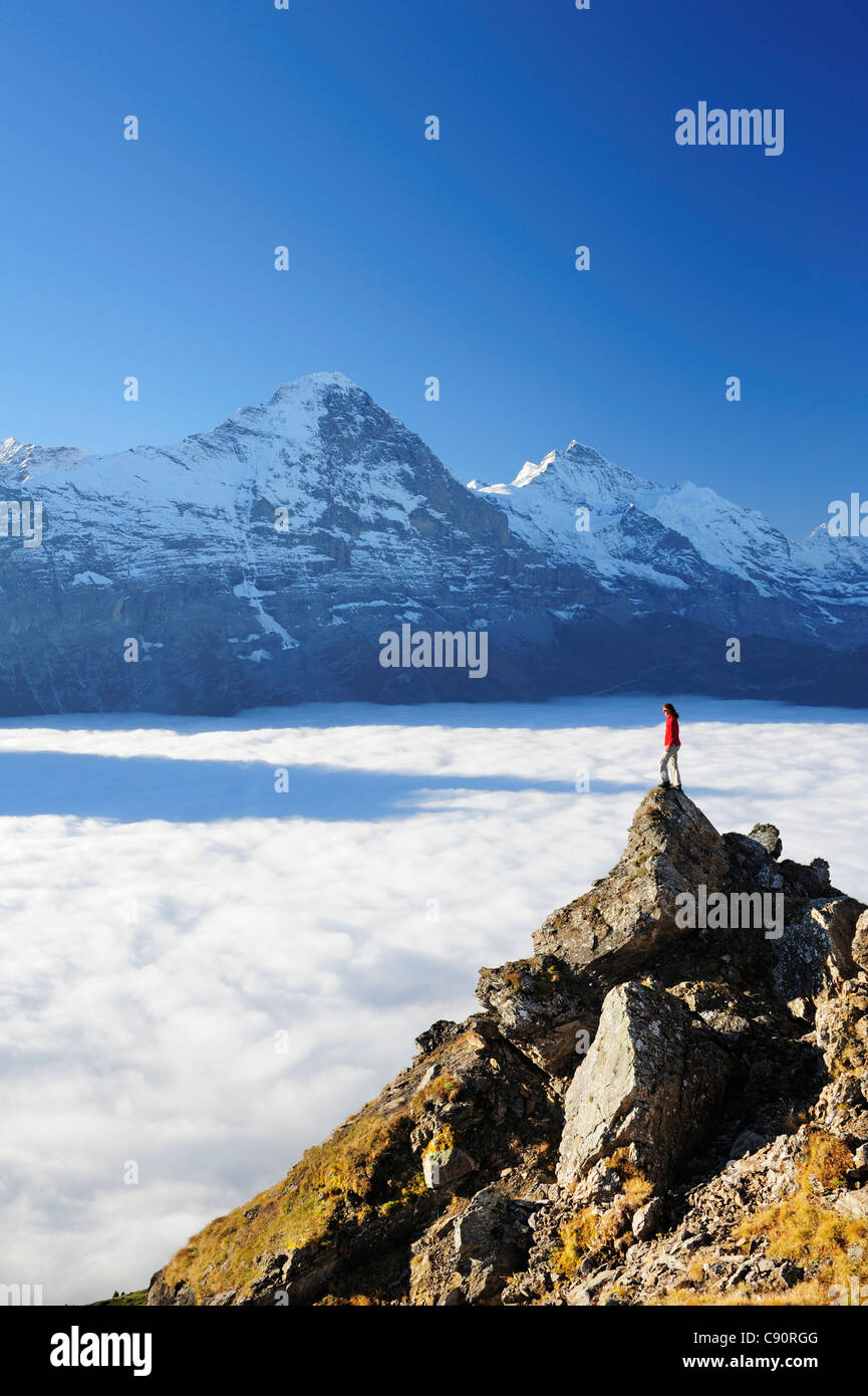 Woman standing on rock and looking towards Eiger and Jungfrau above sea of fog, Bussalp, Grindelwald, UNESCO World Heritage Site Stock Photo
