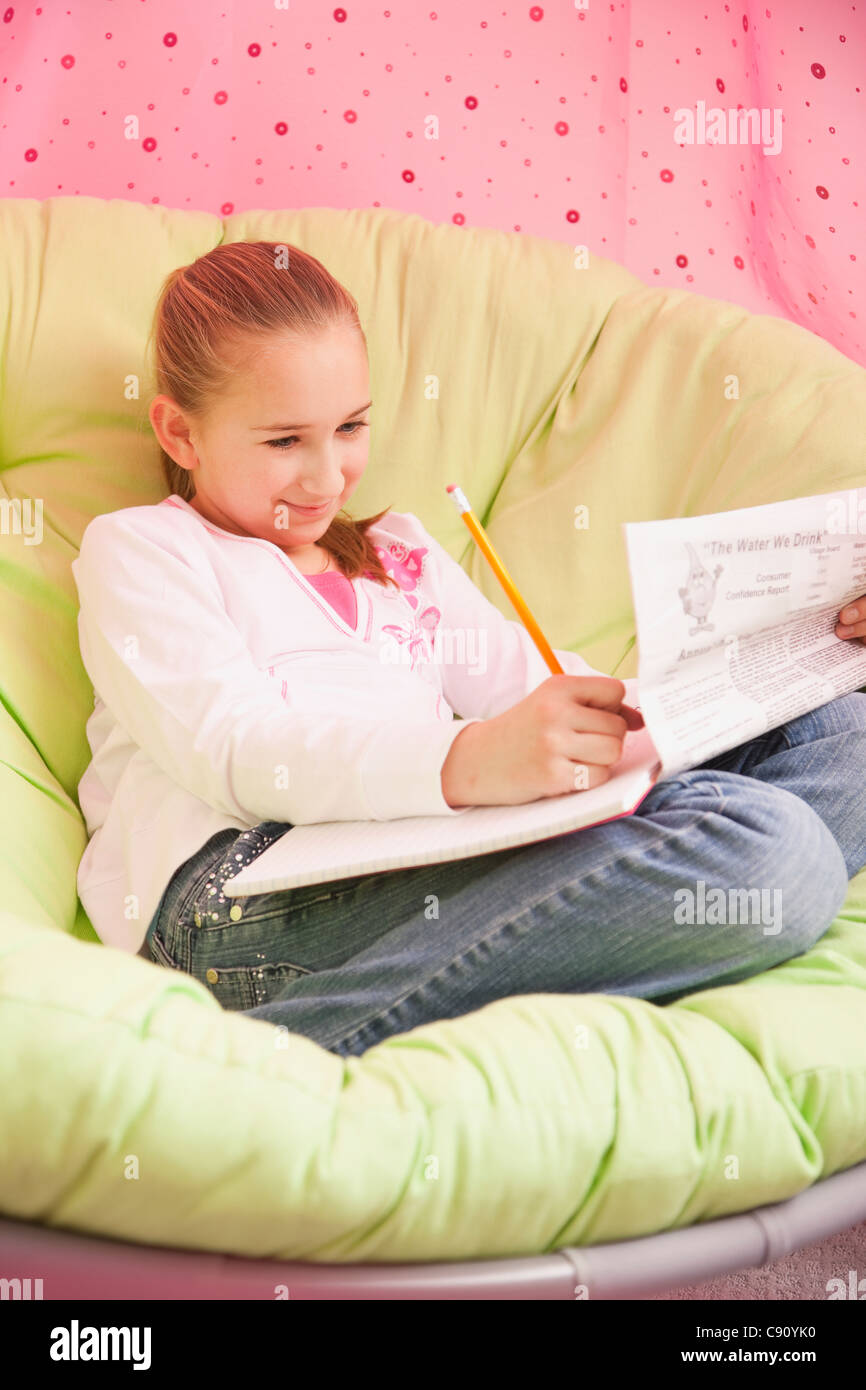 USA, Illinois, Metamora, Girl (10-11) sitting on soft chair and writing Stock Photo