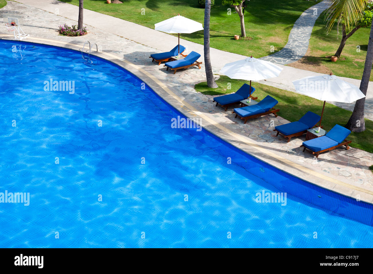 Swimming pool with chaise lounge and sunshade at tropical resort Stock Photo
