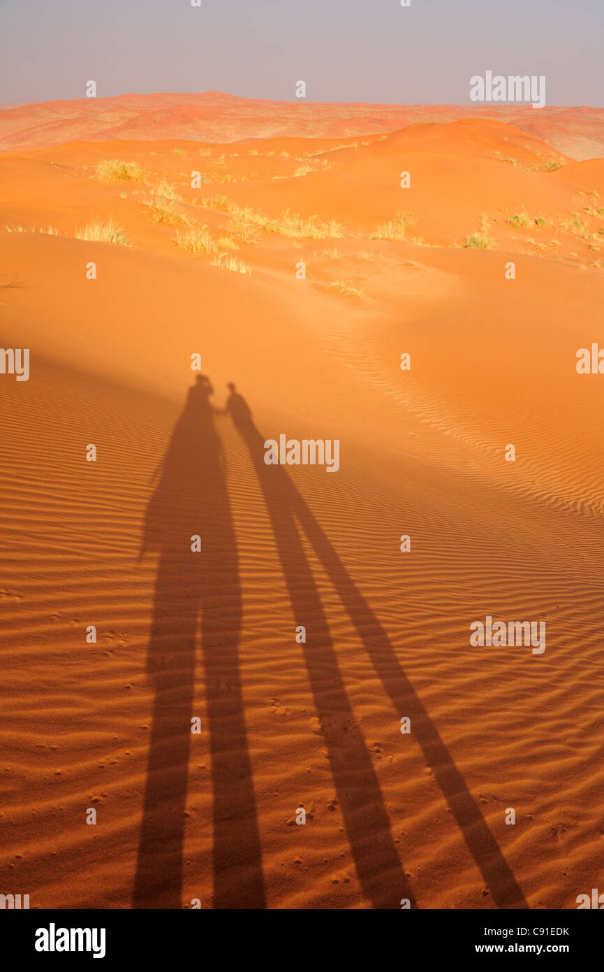 Two people holding hands throwing shadow on red sand dunes, Namib Rand Nature Reserve, Namib