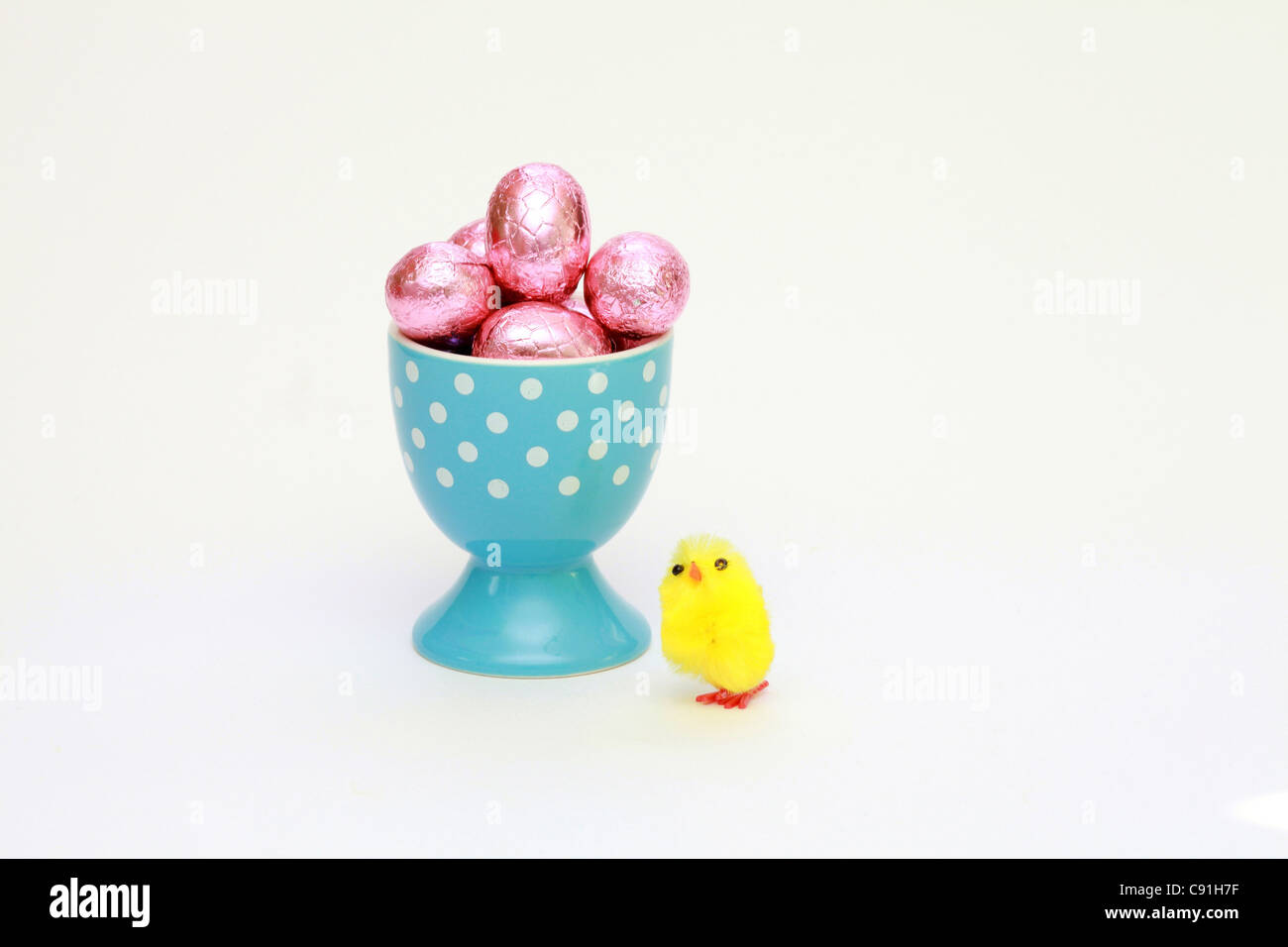 A little fake chicken next to a egg-cup filled with chocolate easter eggs Stock Photo