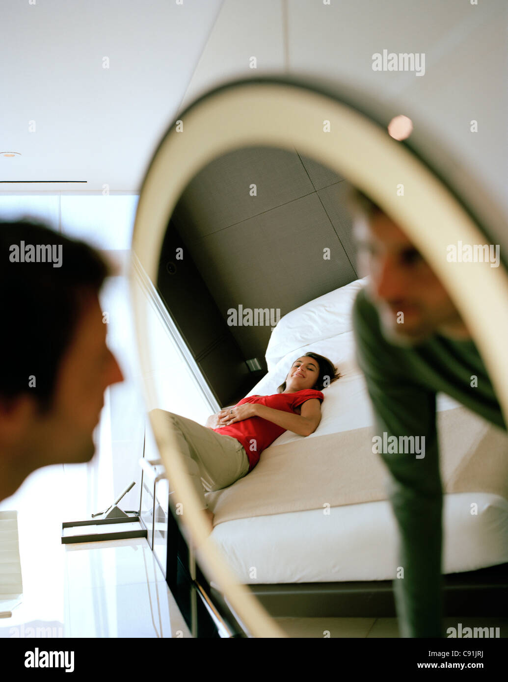 Man looking into the mirror Woman lying on the bed watching Hotel room