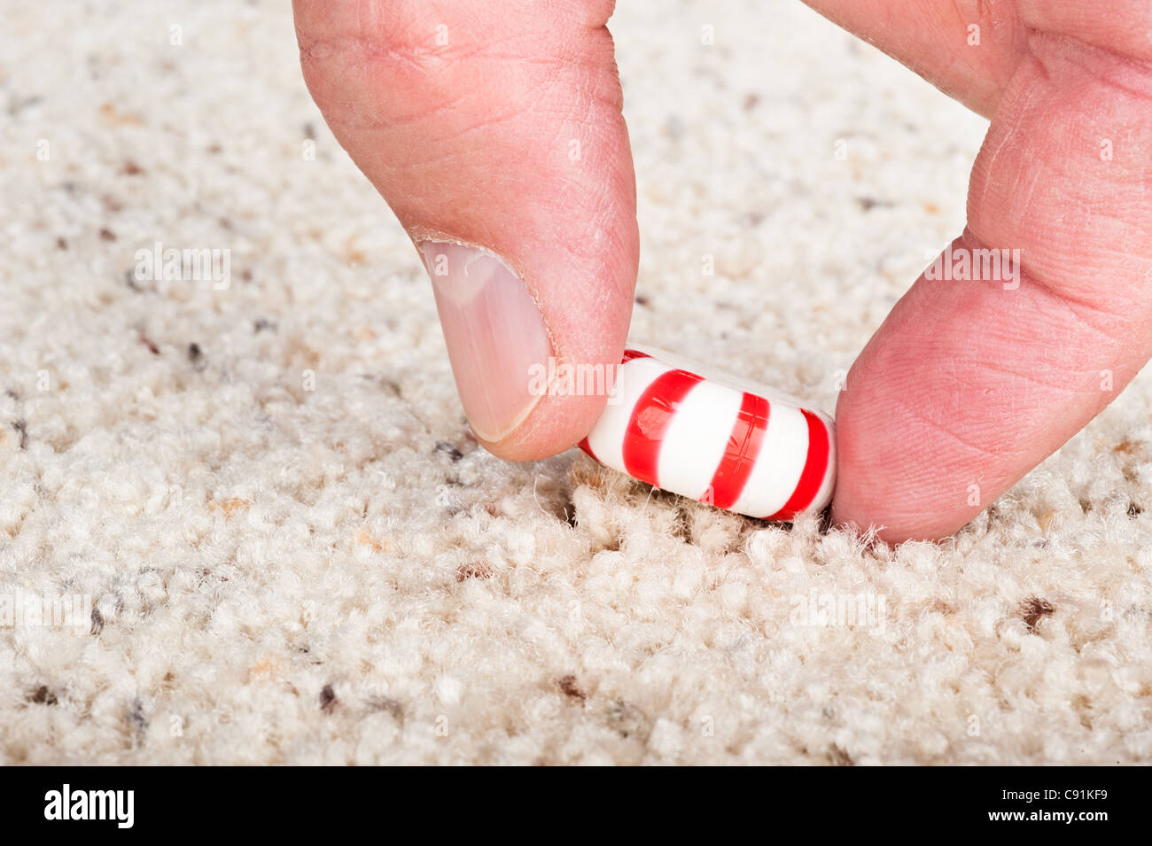 A person pulling a sticky candy mint off the carpet. Stock Photo