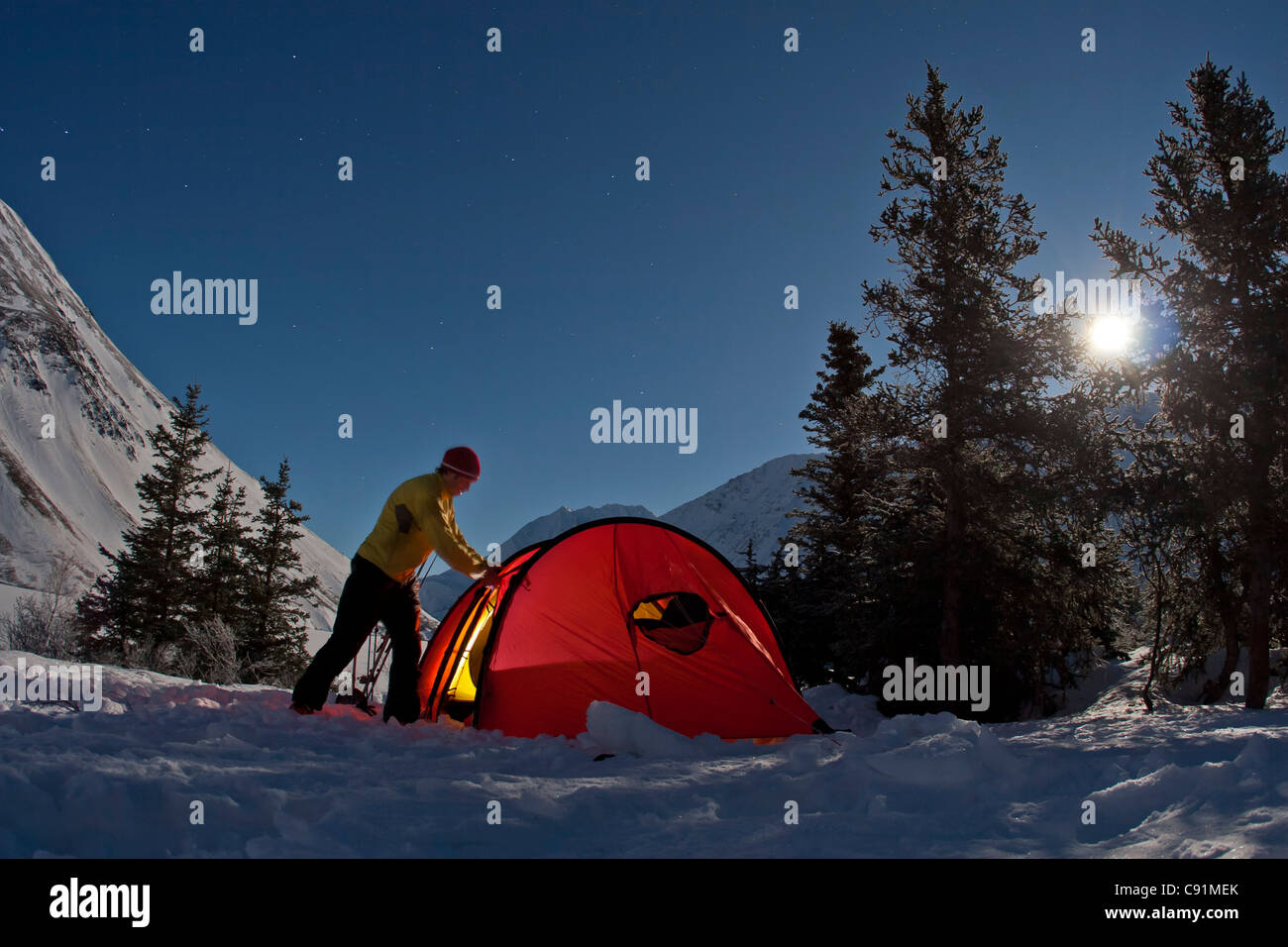 Camper setting up the tent under full moon light at the Crescent Saddle Cabin, Kenai Mountains, Kenai Peninsula, Alaska Stock Photo