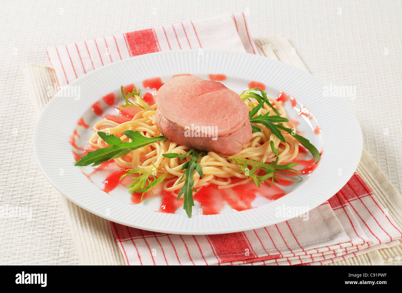 Pork fillet and spaghetti with raspberry balsamic reduction and rocket Stock Photo
