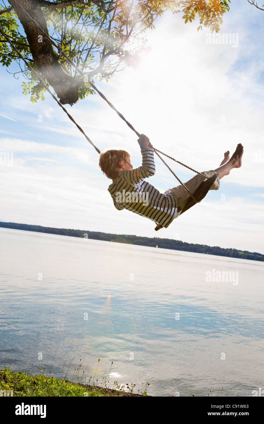 Boy swinging from tree by lake Stock Photo Alamy