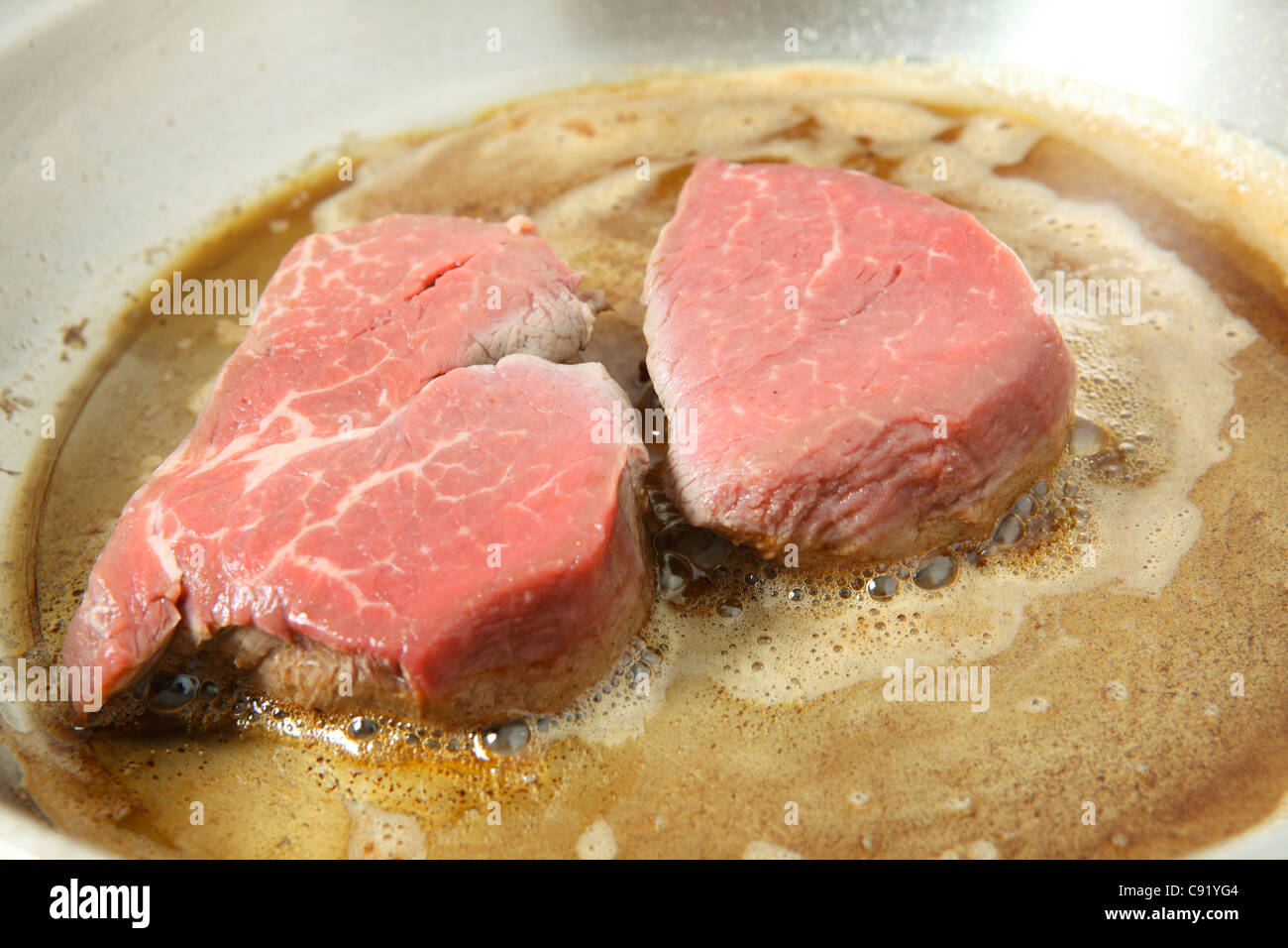 Two filet mignon steaks frying in butter in a steel frying pan Stock