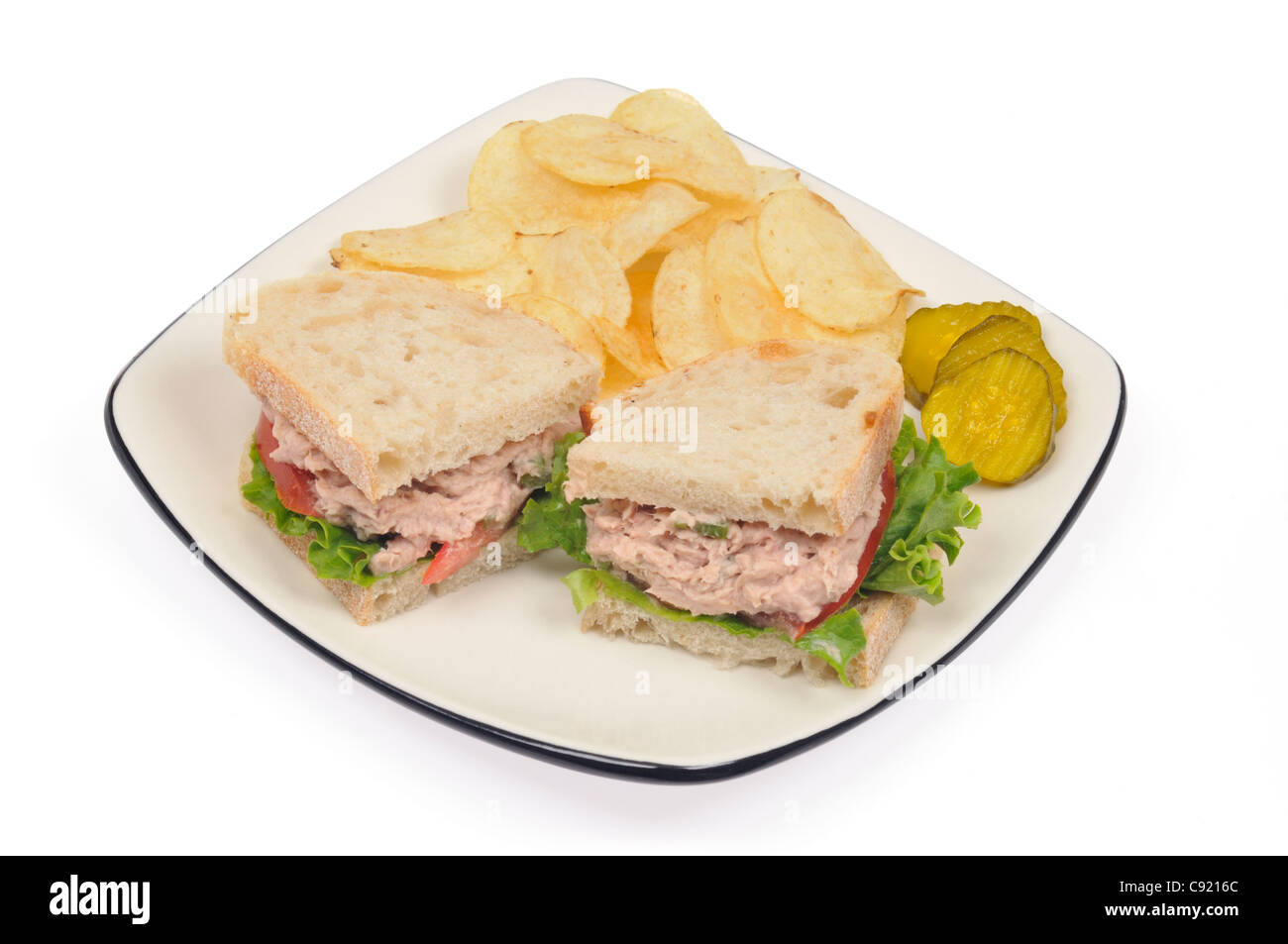 Tuna mayo sandwich on white bread with lettuce, tomato, chips or crisps and pickles on white background. Stock Photo