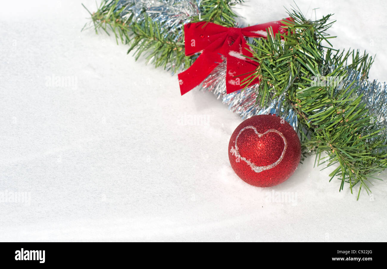 Bright red Christmas ball ornament in snow with a wreath and tinsel Stock Photo