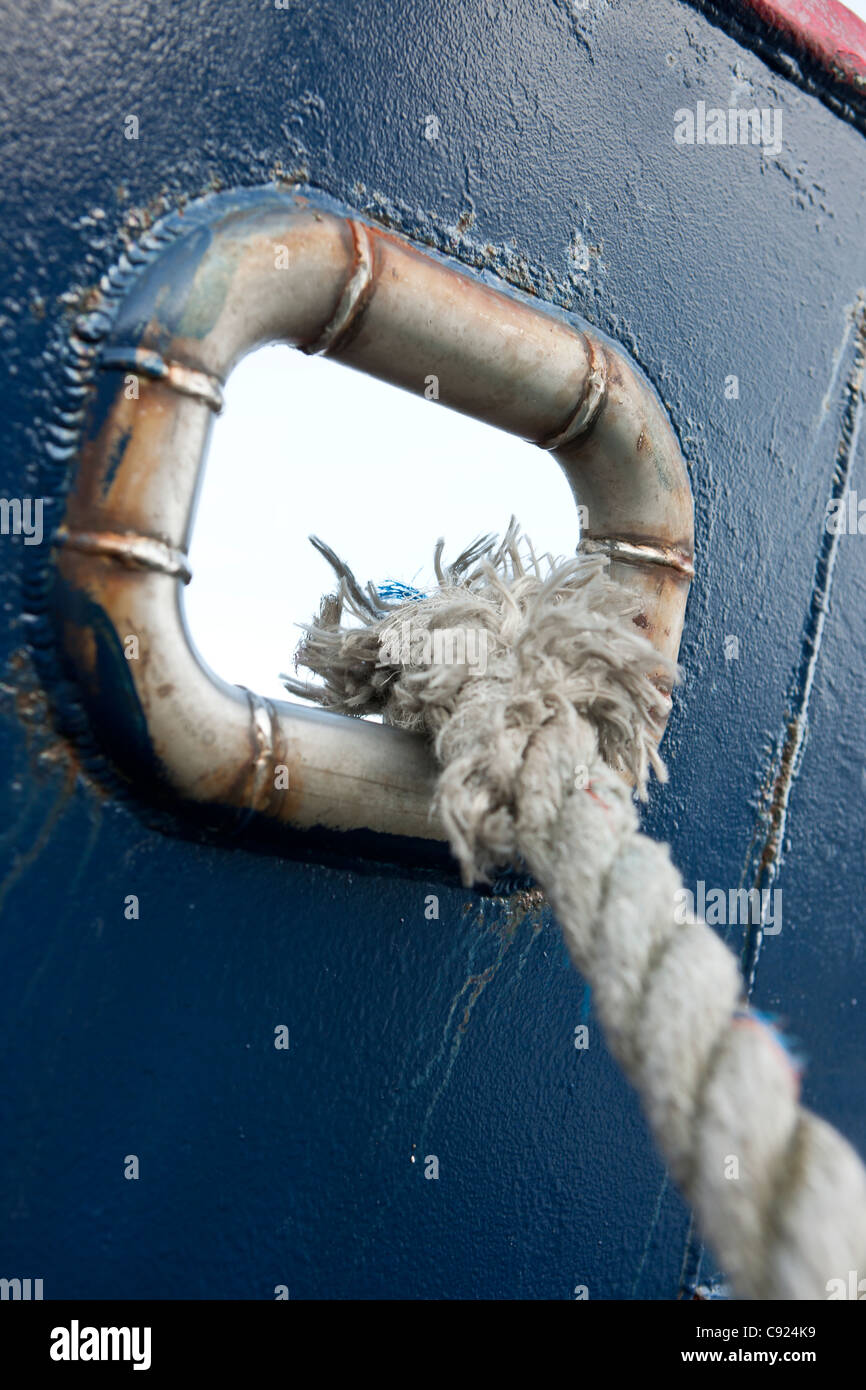 frayed mooring rope through a port hole on blue commercial fishing vessel, Alaska Stock Photo