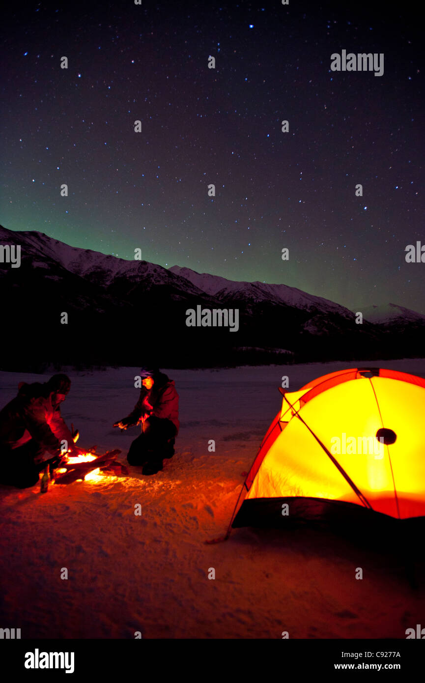 Two men camp on the frozen Eklutna Lake with the Northern Lights overhead, Chugach State Park, Southcentral Alaska, Winter Stock Photo