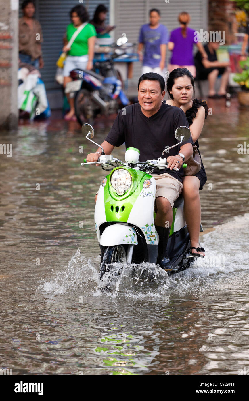 Couple riding motorbike through flood water in Bangkok city centre, Thailand Stock Photo