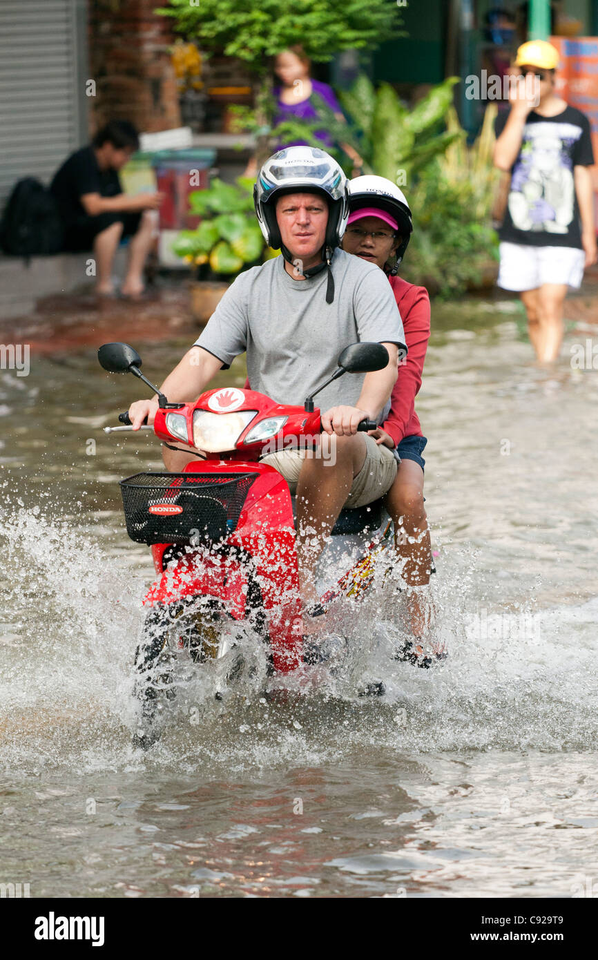 Couple riding a motorbike through flood water in Bangkok city centre, Thailand Stock Photo
