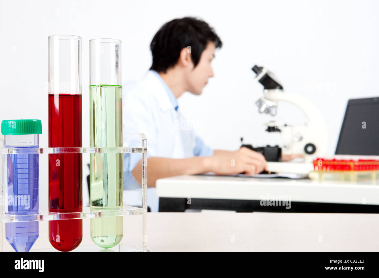 Man sitting in front of microscope writing on paper pad in lab Stock ...