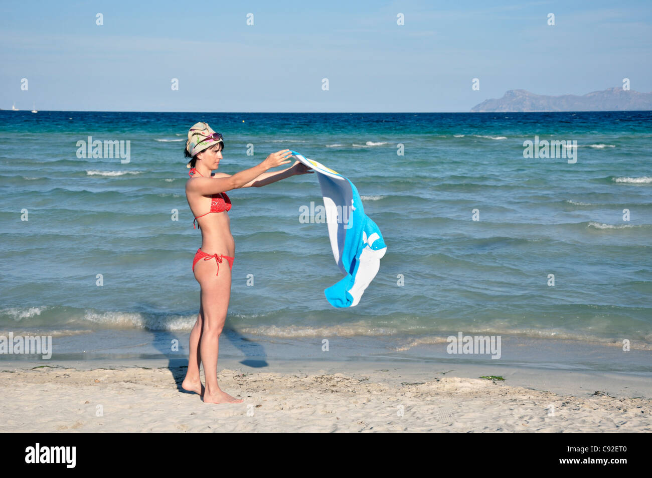 Mid adult woman spreads out towel on beach, Alcudia, Mallorca, Spain, Europe Stock Photo