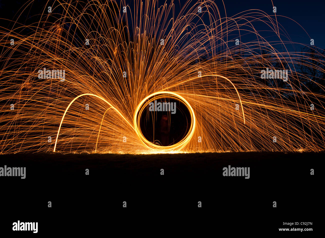 Steel wool spinning, creating gorgeous circular streaks of golden light from burning wire wool inside a whisk attached to wire, or rope. Stock Photo