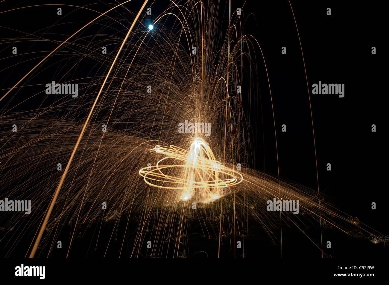 Steel wool spinning, creating gorgeous circular streaks of golden light from burning wire wool inside a whisk attached to wire, or rope. Stock Photo