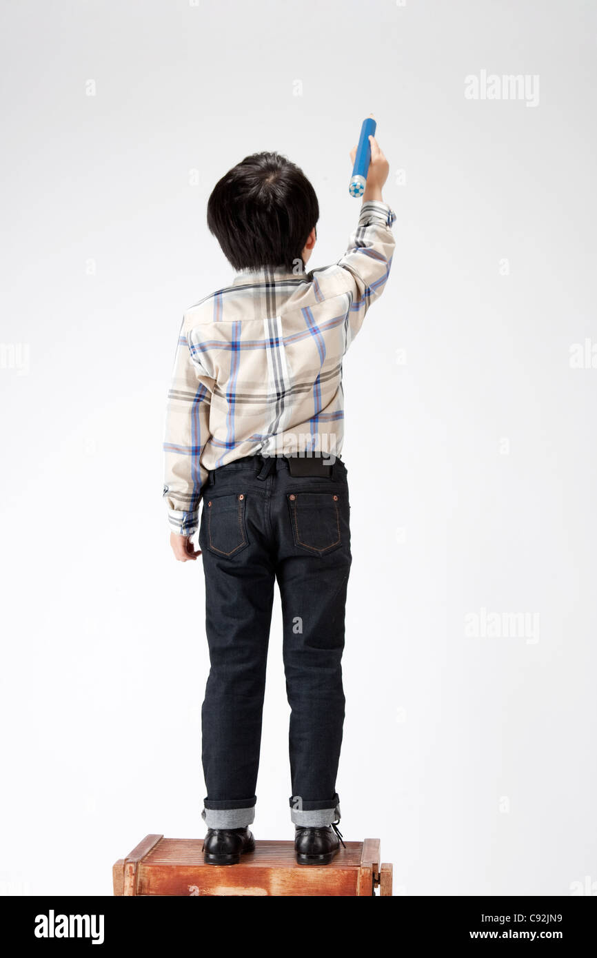 Boy standing on stool holding pencil, rear view Stock Photo Alamy