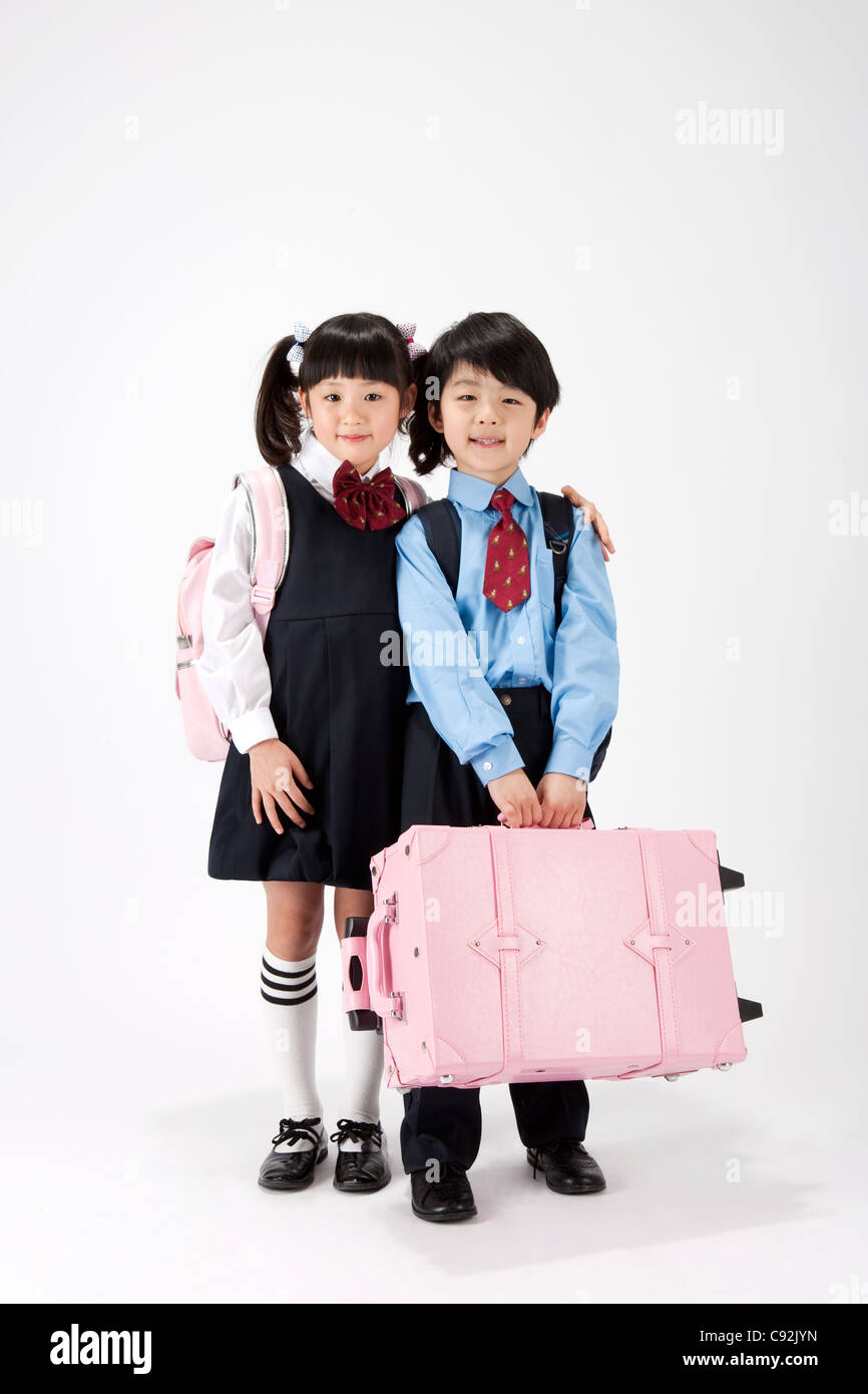 Girl and boy in school uniform with carrying school bag and luggage