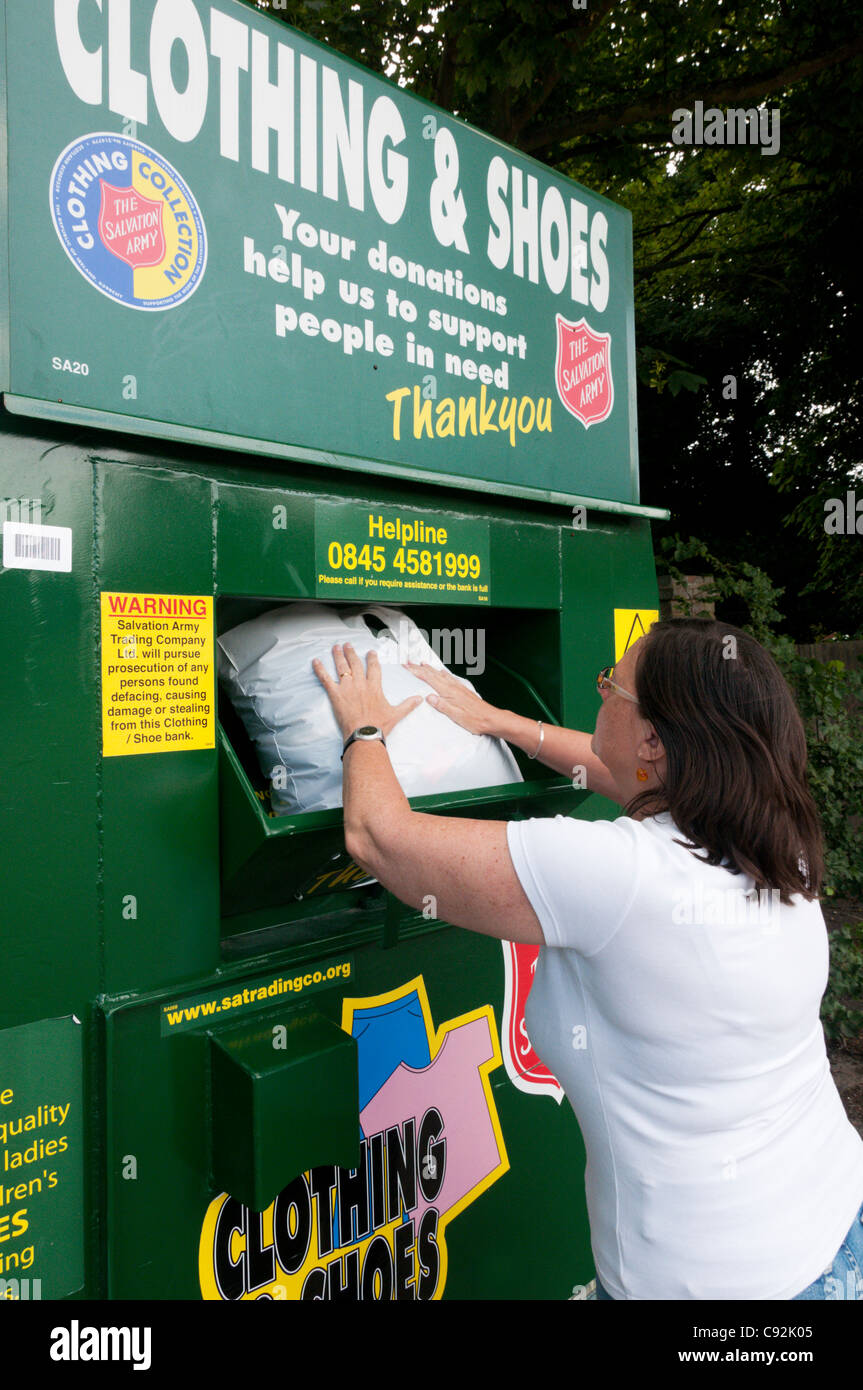 A woman puts a bag of clothing in a Salvation Army charity collection point for unwanted clothing & shoes. Stock Photo