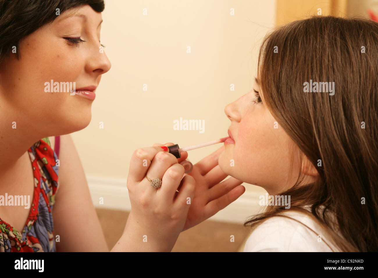 An elder sister applying lip gloss to her younger sister. Stock Photo