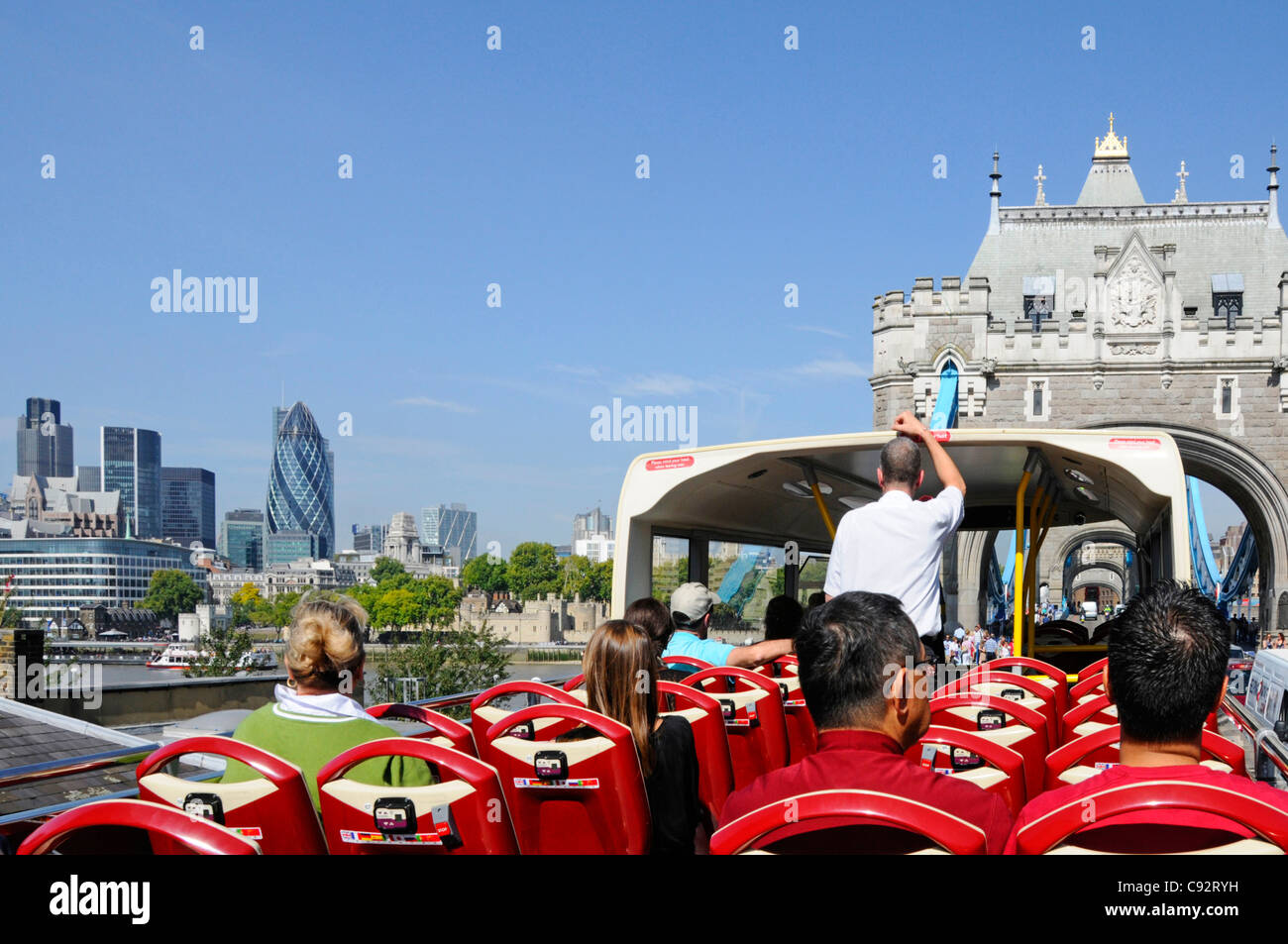 Tourists on double decker open top London sightseeing tour bus with views of Tower Bridge & City of London skyline on a blue sky summer day UK Stock Photo