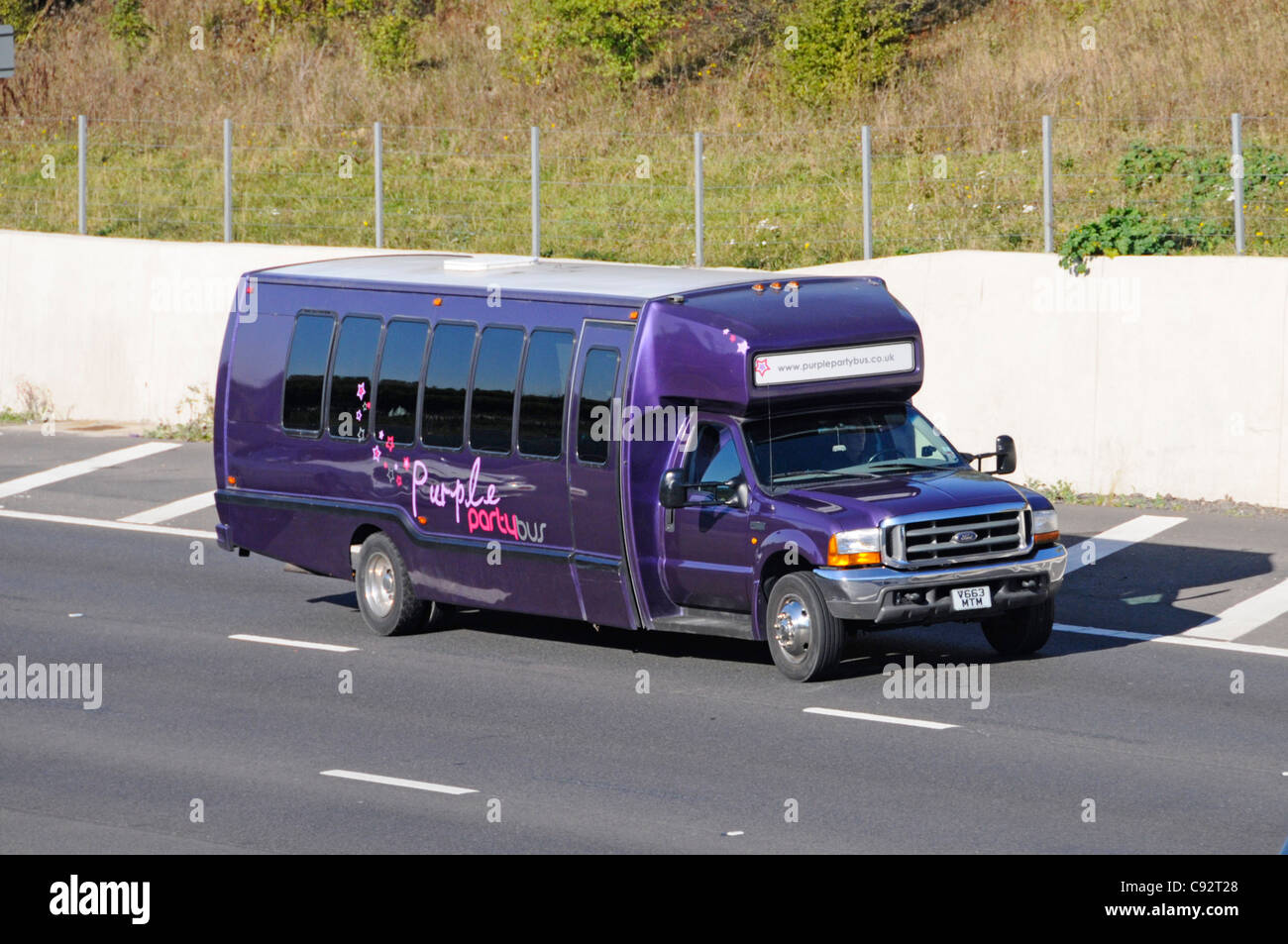Ford Purple Party mini bus fitted with tinted dark passenger windows driving along M25 motorway Essex England UK Stock Photo