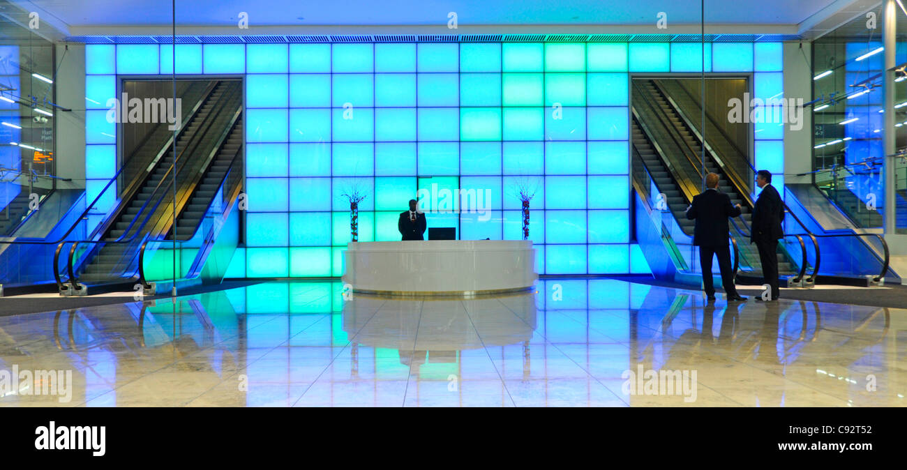 Colourful blue light wall behind reception desk in entrance foyer to office building interior escalators to floors above in City of London England UK Stock Photo