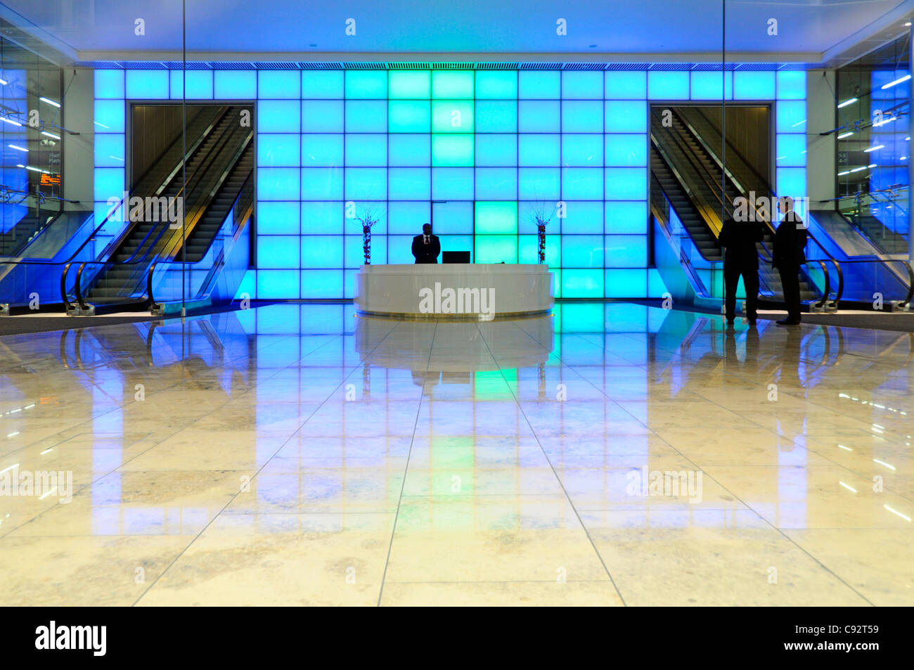 Variable selected colourful blue light wall behind reception desk in entrance foyer to office building with escalators in City of London England UK Stock Photo
