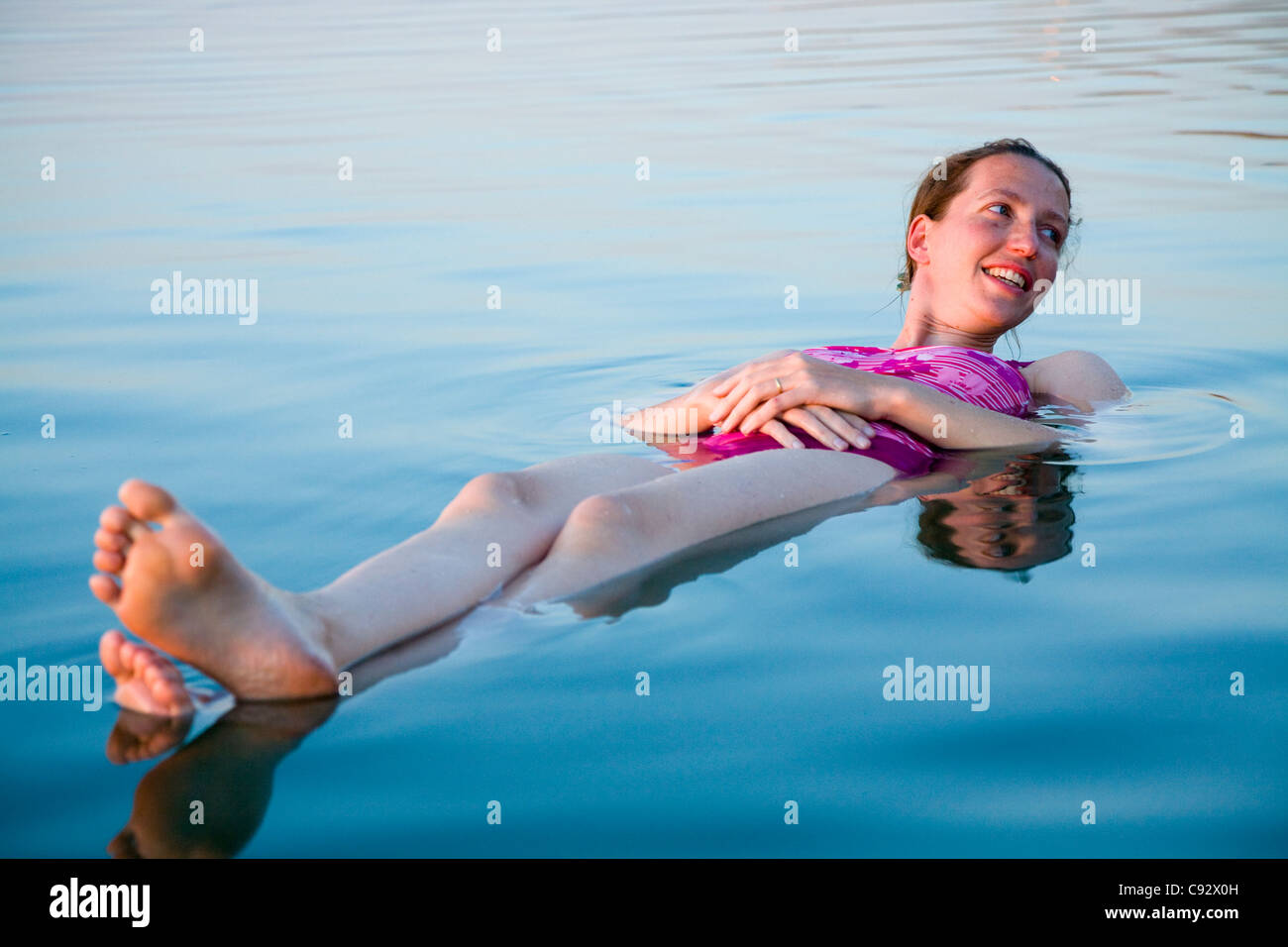 Woman tourist / girl afloat floating / a float on the high salt content / salty saline water of the Dead Sea lake. Stock Photo