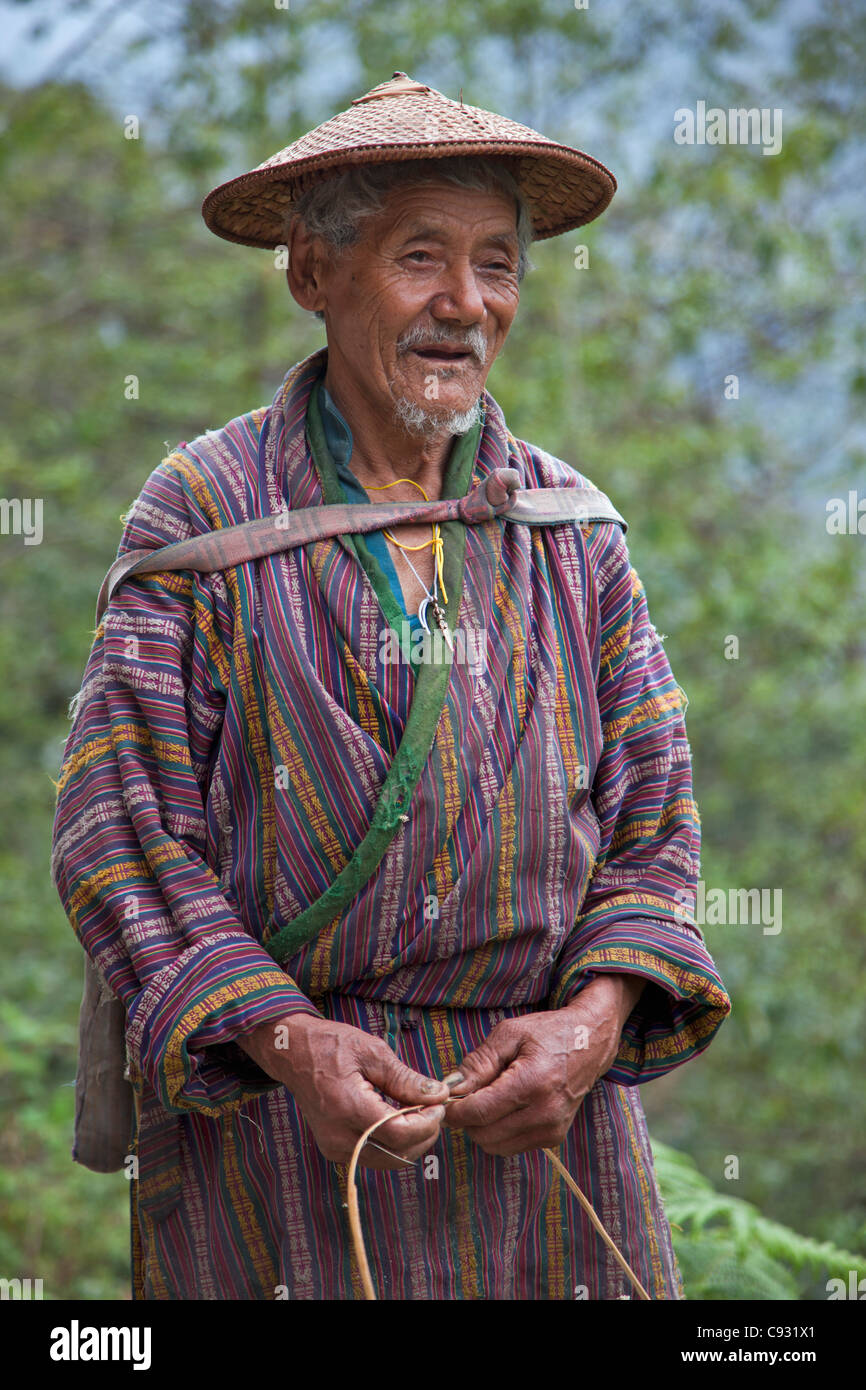 A wizened old farmer near Mongar wears the knee-length national robe called gho and a conical bamboo hat, the belo. Stock Photo