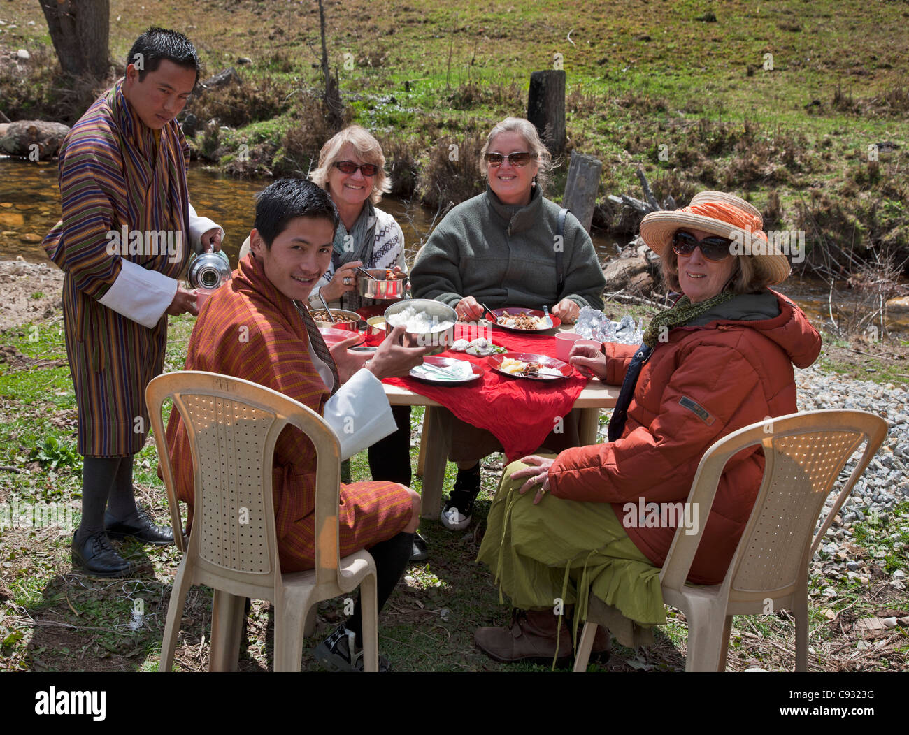 Tourists enjoy a delicious picnic lunch beside a stream in the Chumey Valley with their guide and driver. Stock Photo