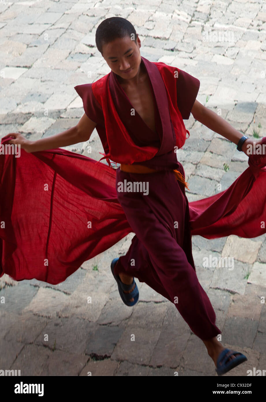 A young monk holds his red robes as he runs across the courtyard of Wangdue Phodrang Dzong (fortress). Stock Photo