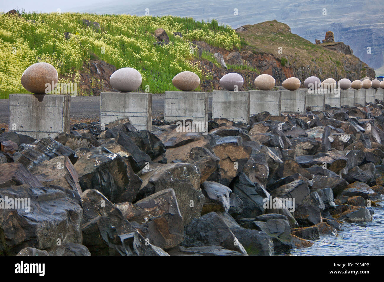 Large stone eggs on plinths lining the fishing harbour at Djupivogur. Stock Photo